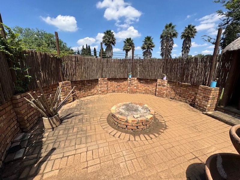Outdoor entertainment area featuring a circular brick fire pit, paved flooring, and a rustic reed privacy fence.