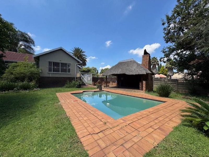 Rear garden featuring a swimming pool with brick paving and a thatched lapa entertainment area.
