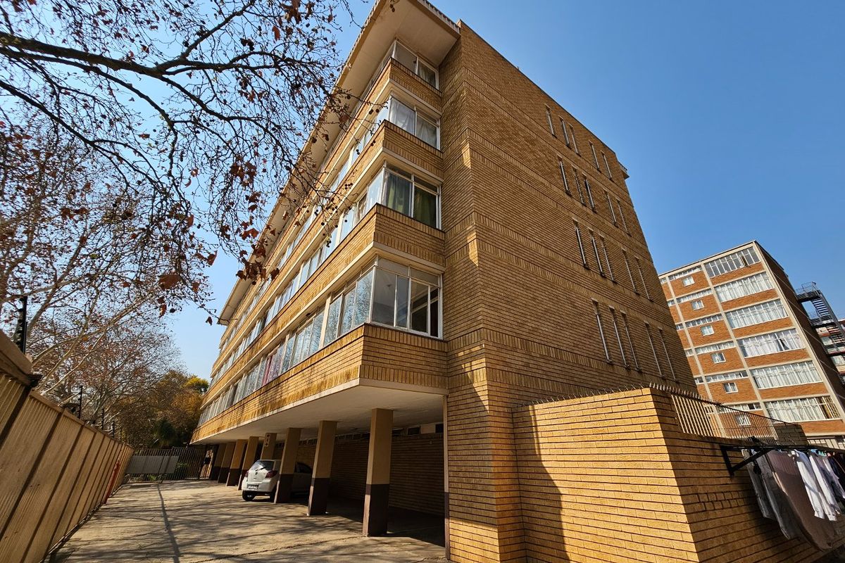 Exterior view of a multi-story brick commercial building featuring a covered ground-level parking area and extensive window banks.