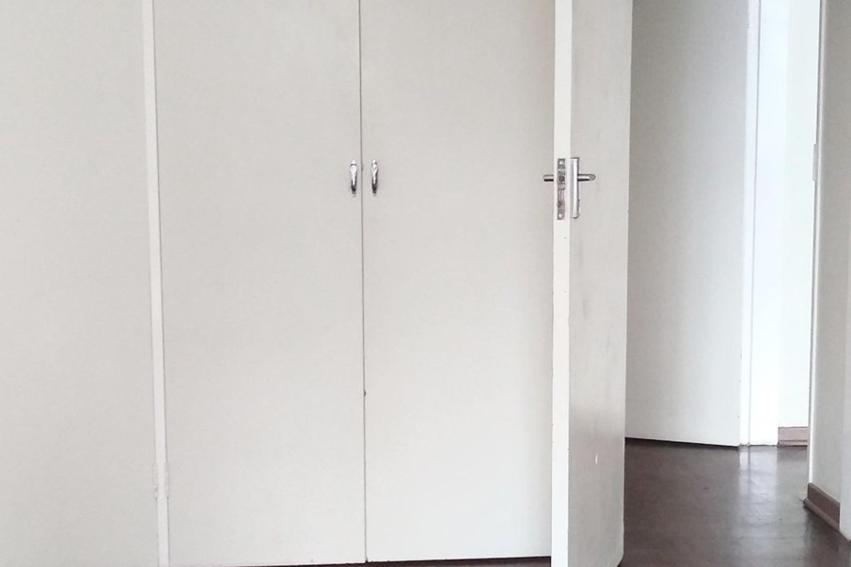 Empty bedroom featuring classic parquet flooring and extensive floor-to-ceiling built-in cupboards with white cabinetry.