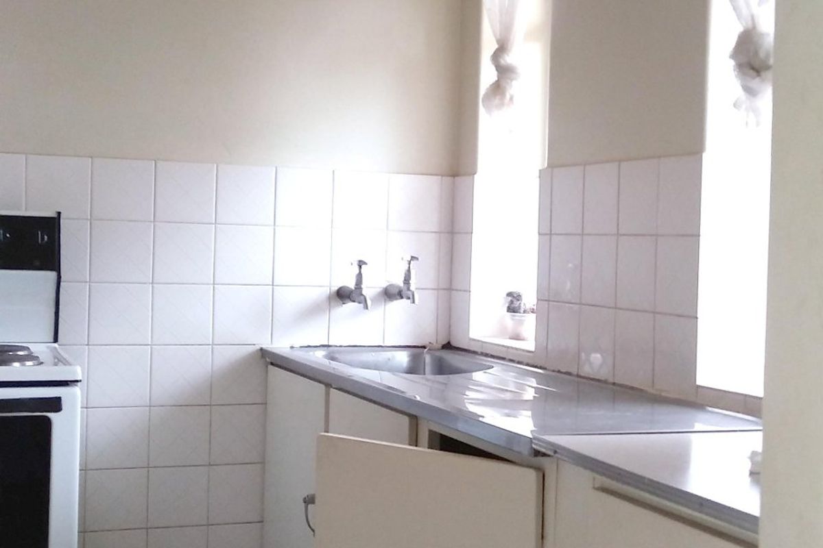 A dated kitchen featuring tiled splashbacks, stainless steel sink, and built-in cabinetry with a damaged cabinet door.