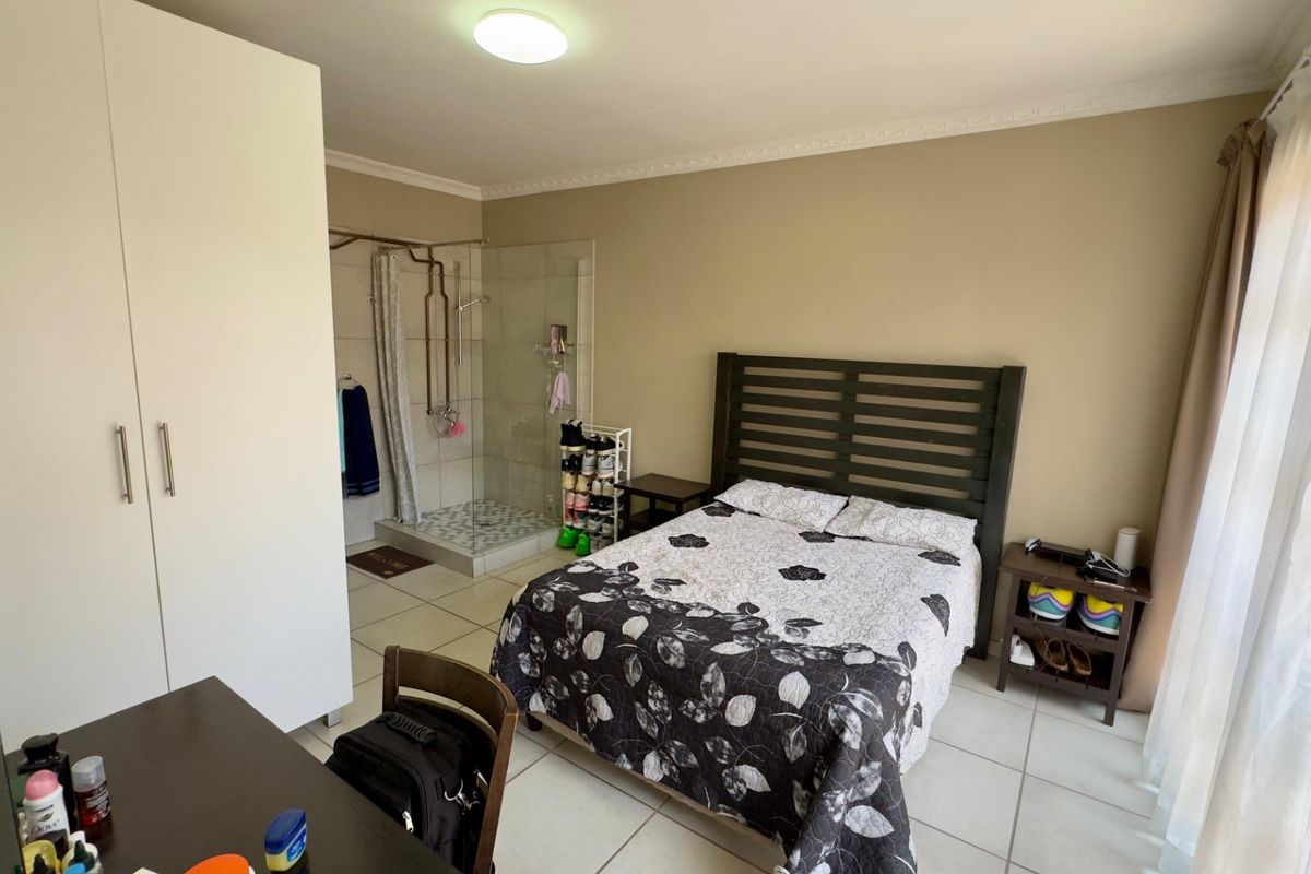 A bedroom featuring an en-suite shower area with glass enclosure, tiled flooring, and built-in wardrobe cabinetry.