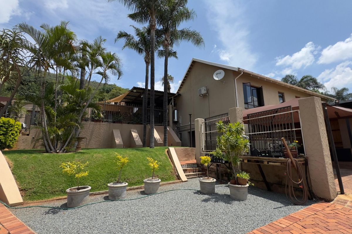 A view of the rear exterior of the house, featuring a landscaped garden, terraced lawn, paved driveway, and a covered patio area.