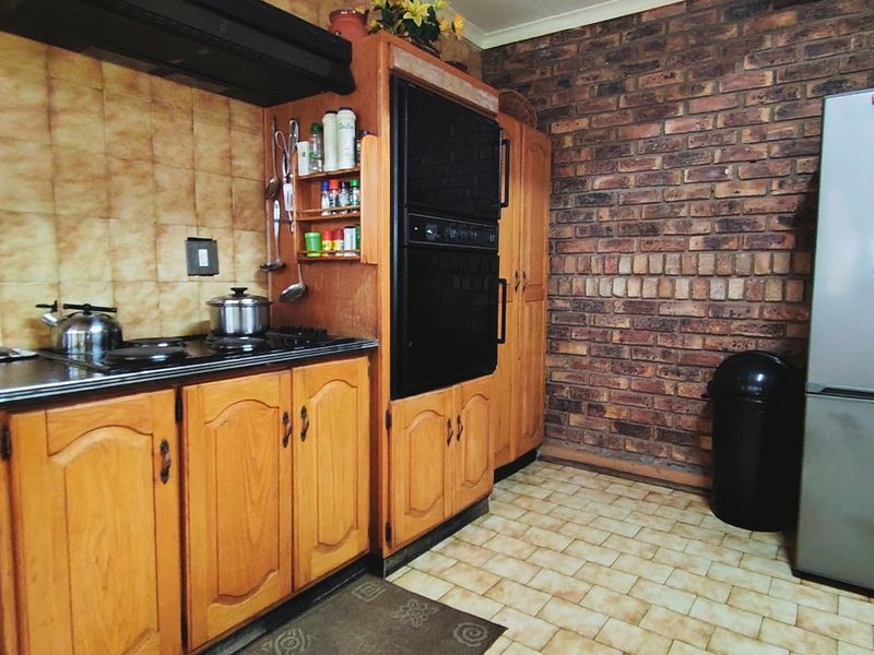 A functional kitchen featuring wooden cabinetry, an integrated oven, extractor fan, and a distinctive exposed brick wall with tiled flooring.