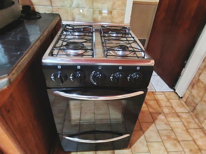 A kitchen area featuring a freestanding gas stove, tiled splashback, and traditional wooden cabinetry with tiled flooring.