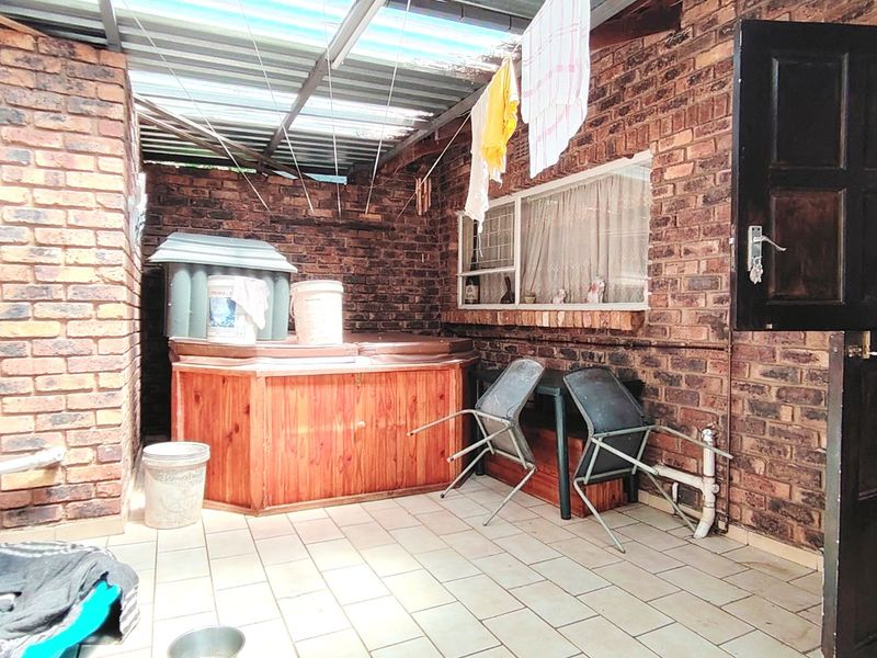 A covered outdoor patio area featuring exposed brick walls, tiled flooring, and a stable door, providing a functional space for outdoor utility or relaxation.