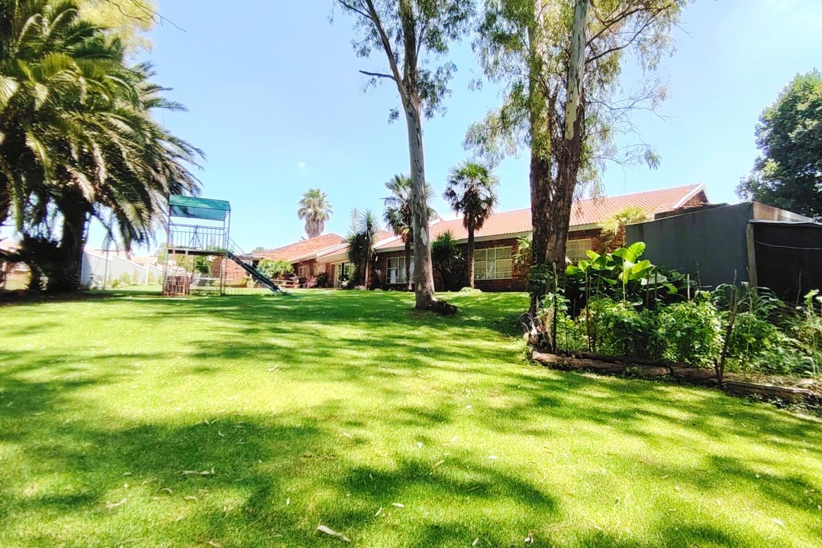 Spacious rear garden featuring a well-maintained lawn, mature trees, and a view of the property's rear brick facade with a tiled roof.