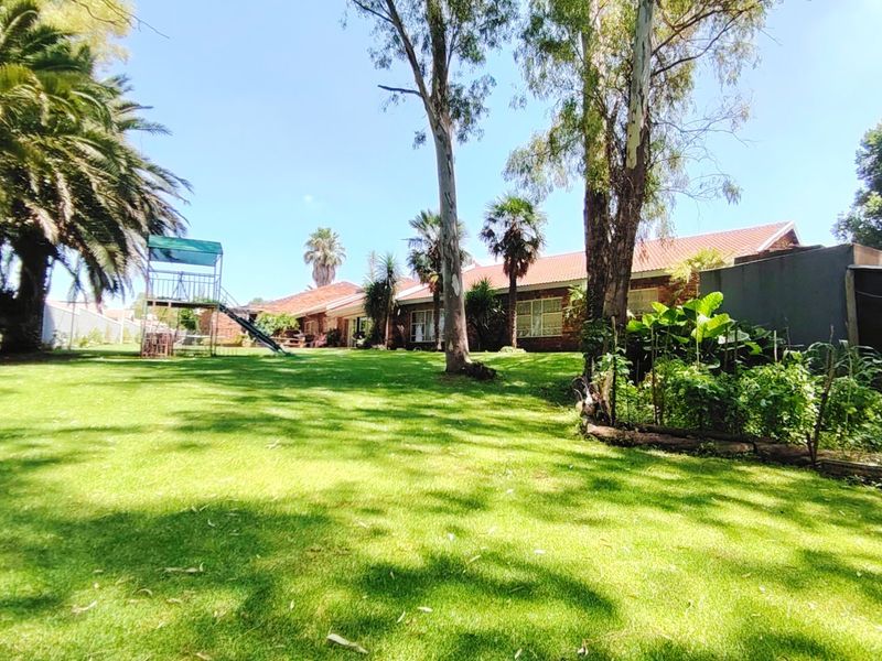 Spacious rear garden featuring a well-maintained lawn, mature trees, and a view of the property's rear brick facade with a tiled roof.