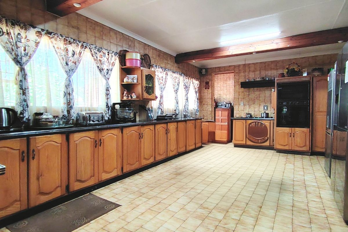 A spacious kitchen featuring extensive wooden cabinetry, built-in oven, cooktop, tiled flooring, and exposed wooden ceiling beams.