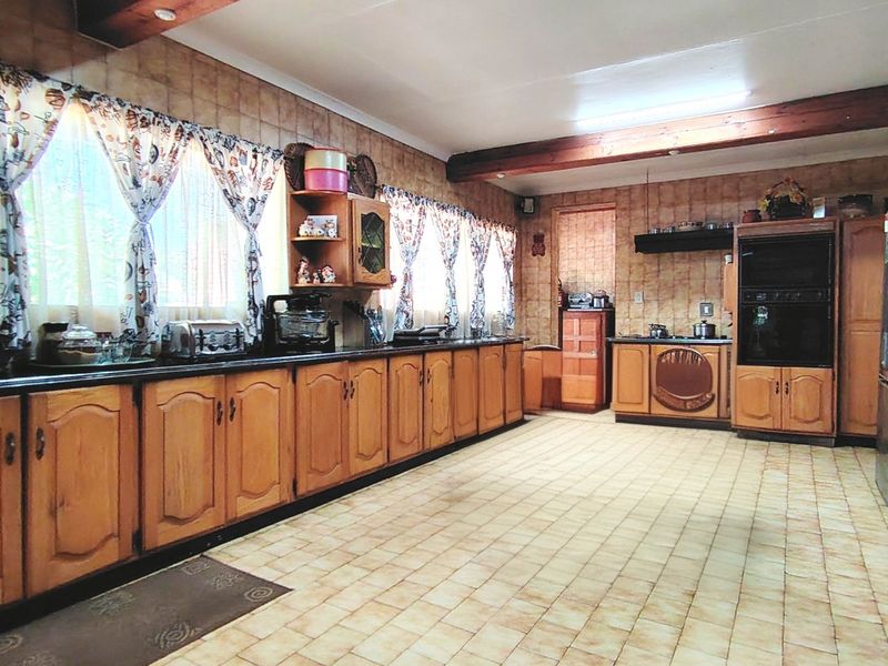 A spacious kitchen featuring extensive wooden cabinetry, built-in oven, cooktop, tiled flooring, and exposed wooden ceiling beams.