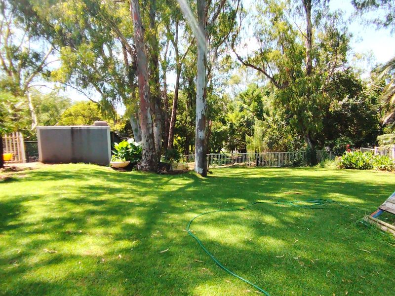 A spacious, well-established garden area featuring mature trees, a manicured lawn, and secure perimeter fencing, offering a private outdoor setting.