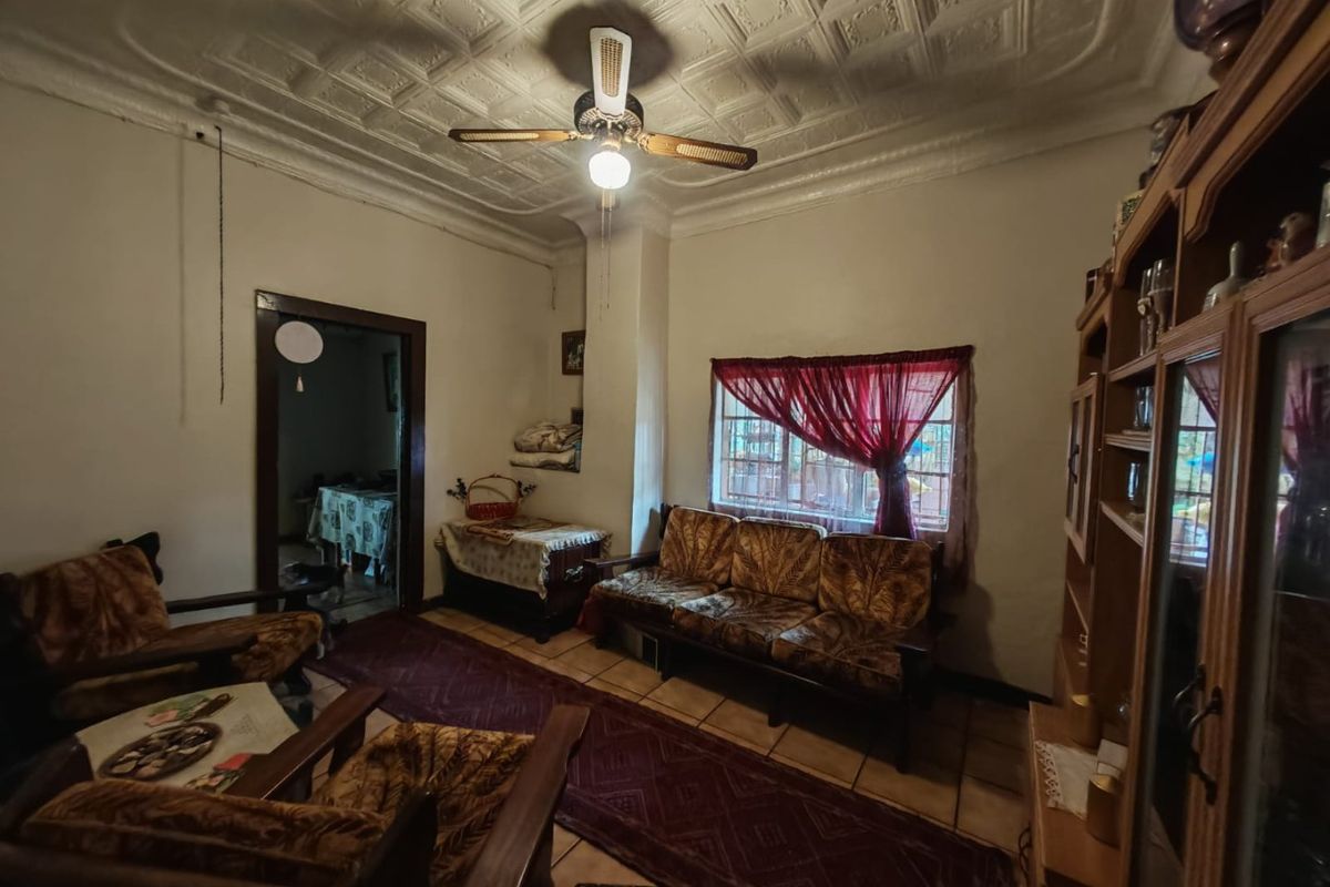 A living room featuring a traditional pressed metal ceiling, ceiling fan, and tiled flooring, offering a dated aesthetic ready for modernization.