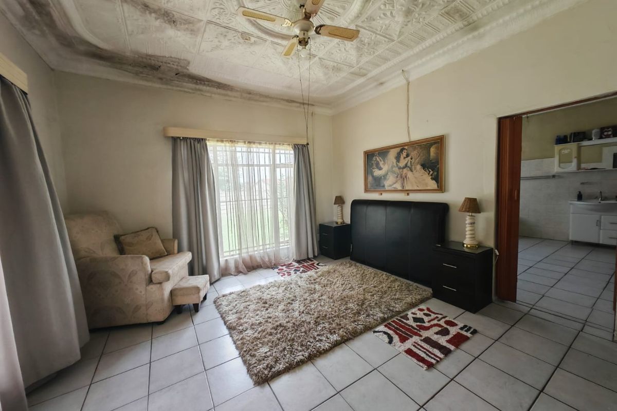 Bedroom featuring tiled flooring, an ornate pressed metal ceiling with a ceiling fan, and security bars on the window. Requires ceiling repair.