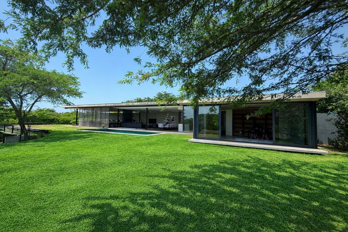 A modern rear exterior view featuring a swimming pool, expansive lawn, and large sliding glass doors connecting the indoor living space to the garden.