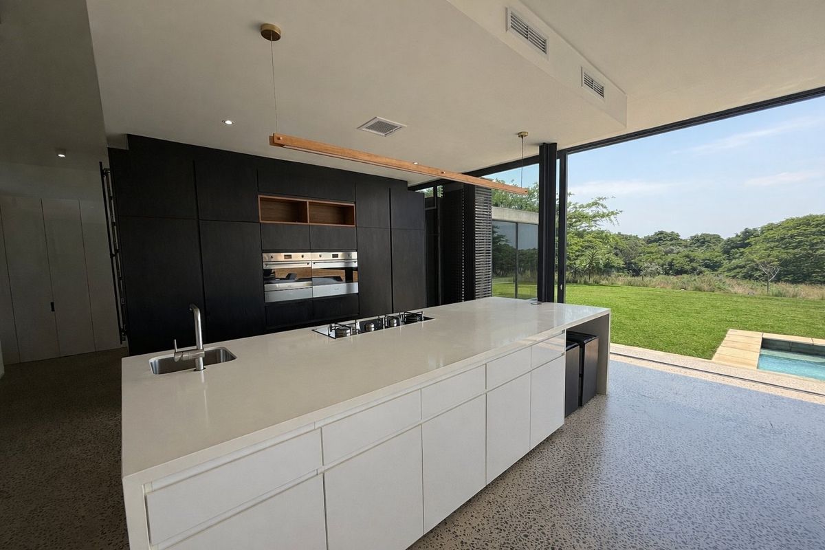 Modern open-plan kitchen featuring a large island with stone countertops, built-in appliances, and seamless indoor-outdoor flow to the garden and pool area.