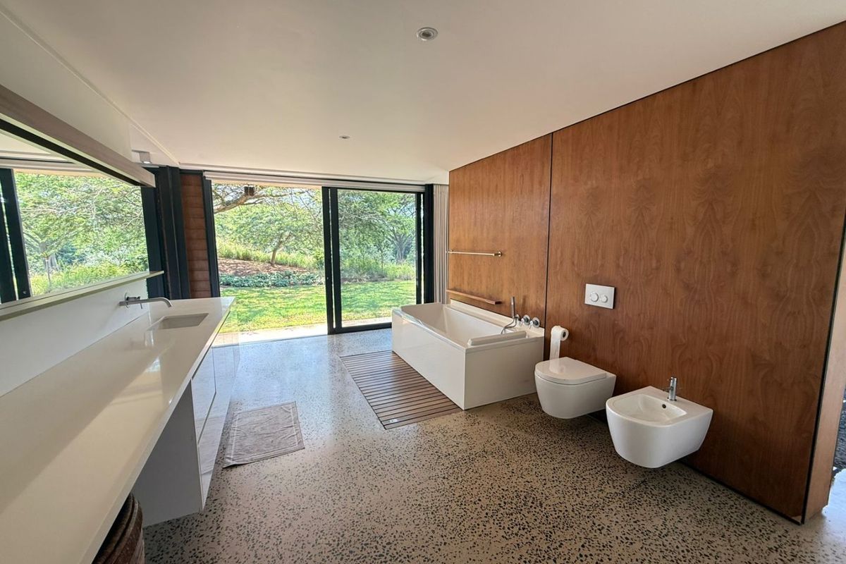 Modern, spacious bathroom featuring a built-in bathtub, wall-mounted toilet, bidet, and a sleek vanity, with large sliding doors opening to a garden view.
