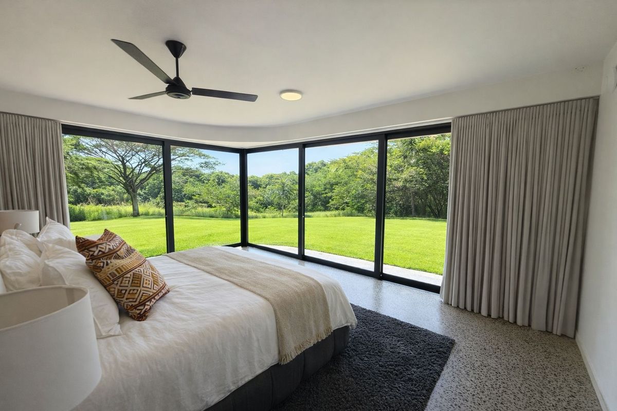 Modern bedroom featuring expansive corner glass sliding doors that provide seamless indoor-outdoor flow and panoramic views of the lush green garden.