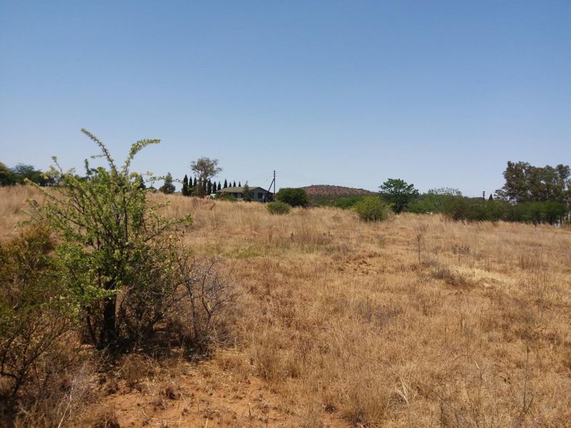A view of a vacant residential plot featuring dry grass and native vegetation with distant structures and power lines visible.