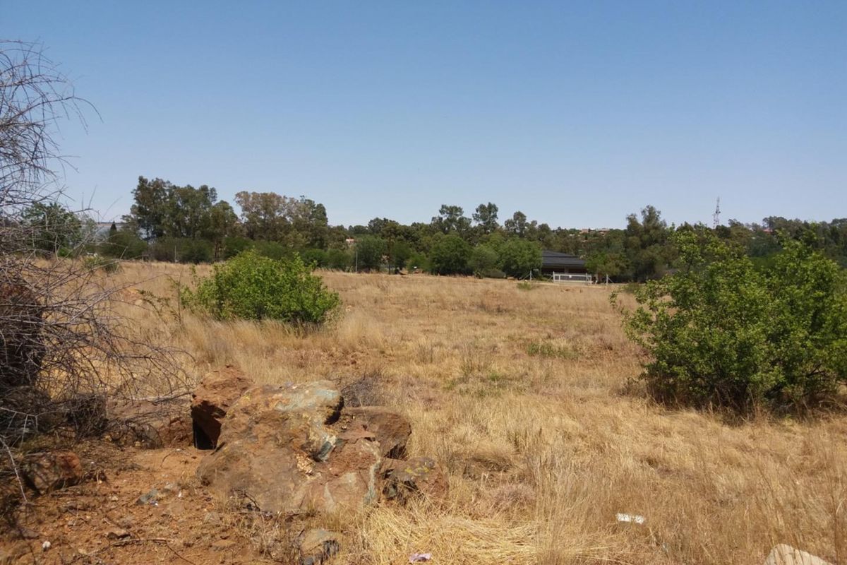A view of a vacant residential plot featuring natural terrain, native shrubs, and rock formations under a clear sky.