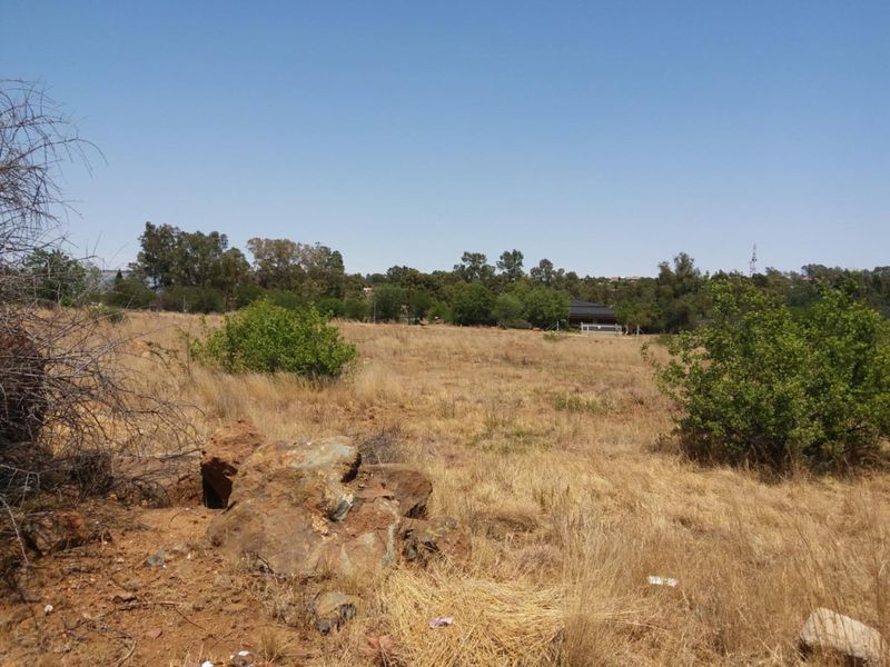 A view of a vacant residential plot featuring natural terrain, native shrubs, and rock formations under a clear sky.