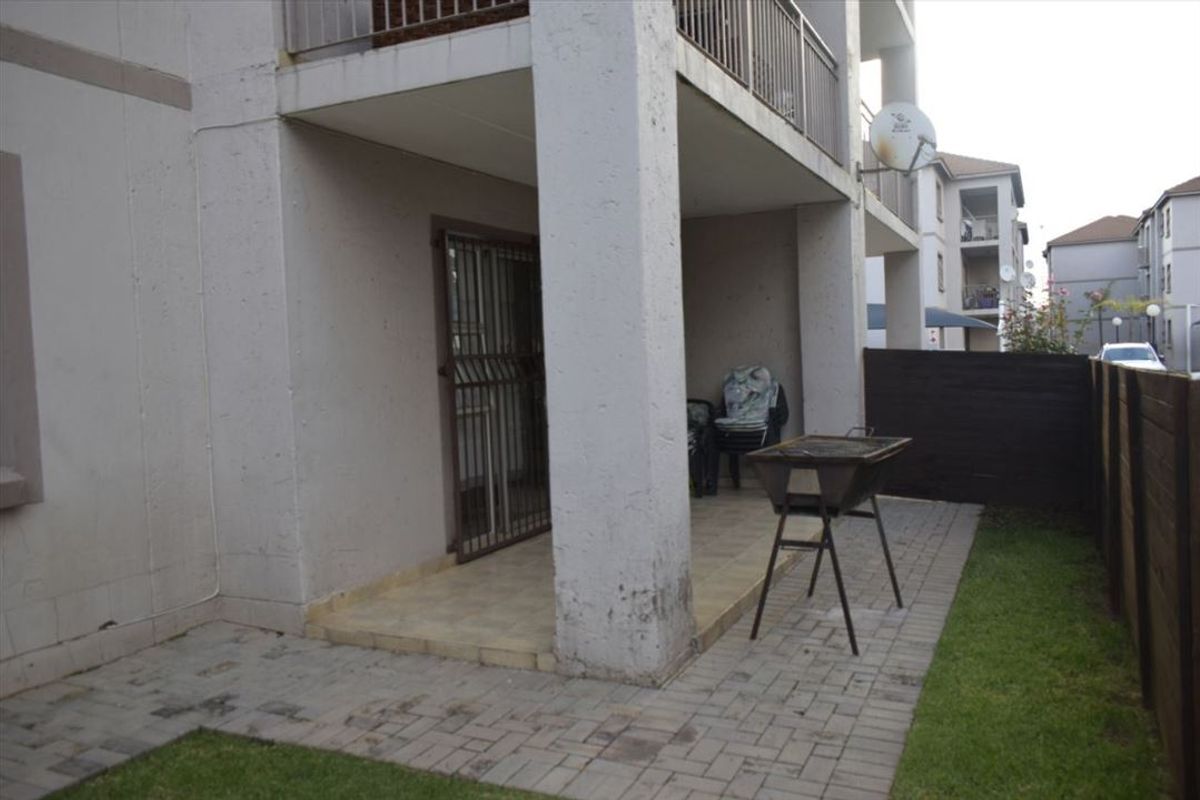 A ground floor paved patio area featuring concrete support pillars, a security gate, and a timber boundary fence.