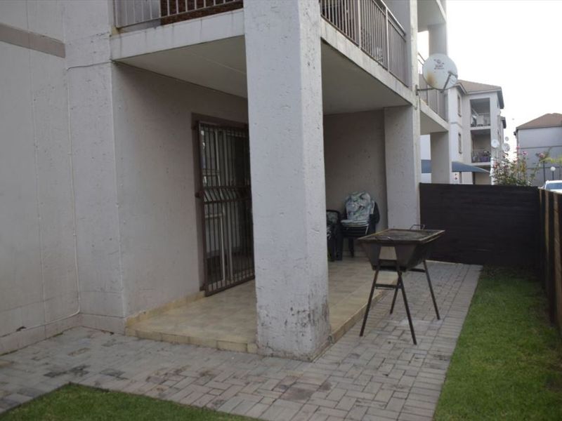 A ground floor paved patio area featuring concrete support pillars, a security gate, and a timber boundary fence.