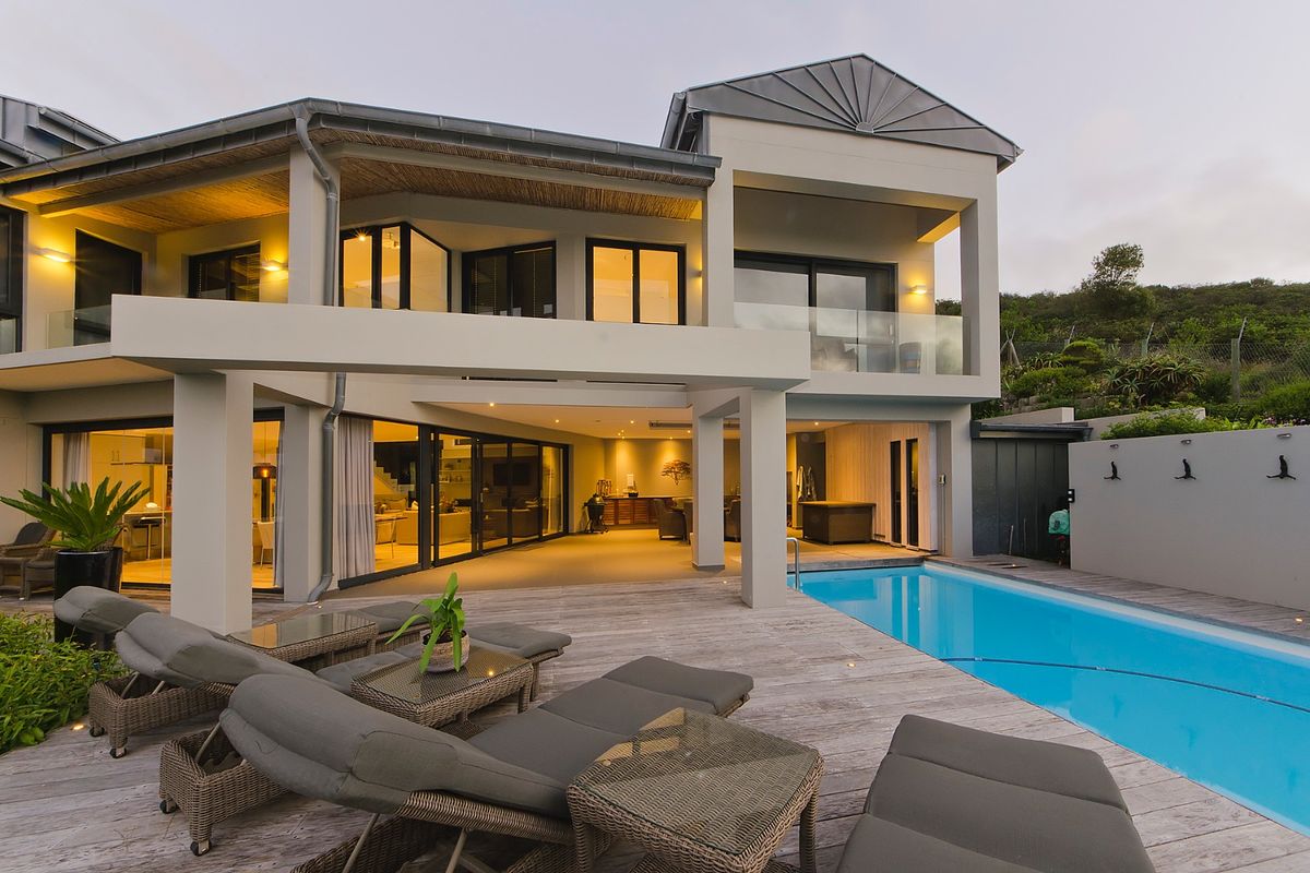 Modern rear elevation featuring a swimming pool, expansive timber decking, and a spacious covered patio area with integrated lighting and large sliding glass doors.