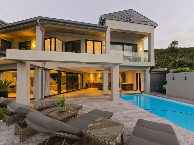Modern rear elevation featuring a swimming pool, expansive timber decking, and a spacious covered patio area with integrated lighting and large sliding glass doors.