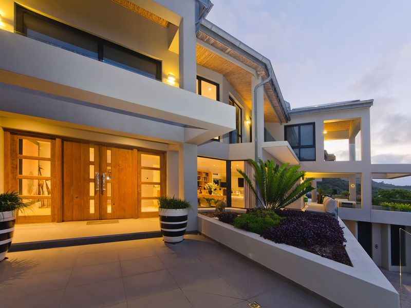 A striking modern architectural facade featuring double timber entrance doors, tiled patio, and integrated lighting, showcasing a high-end contemporary design.