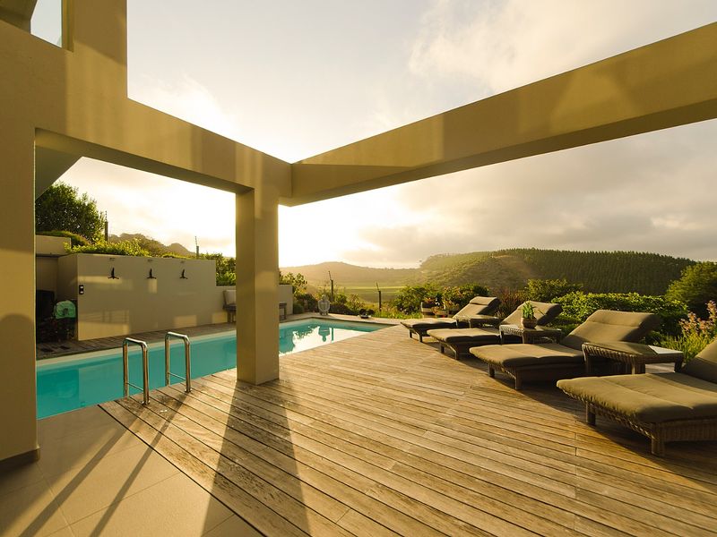 A spacious outdoor pool area featuring timber decking, a swimming pool, and a covered patio with scenic hillside views.
