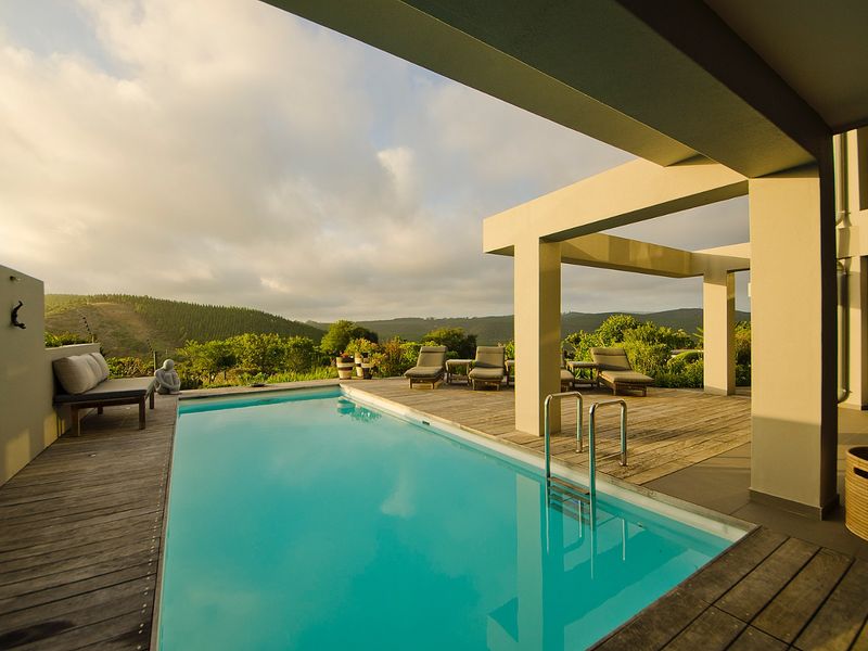 A well-maintained outdoor pool area featuring timber decking, a concrete pergola, and scenic landscape views.