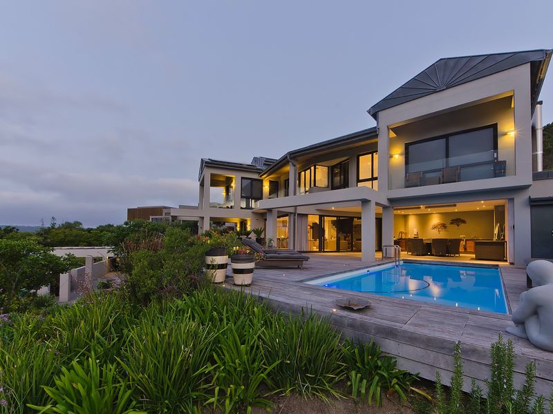A modern multi-level residence featuring a swimming pool, expansive timber decking, and covered outdoor entertainment areas with integrated lighting.