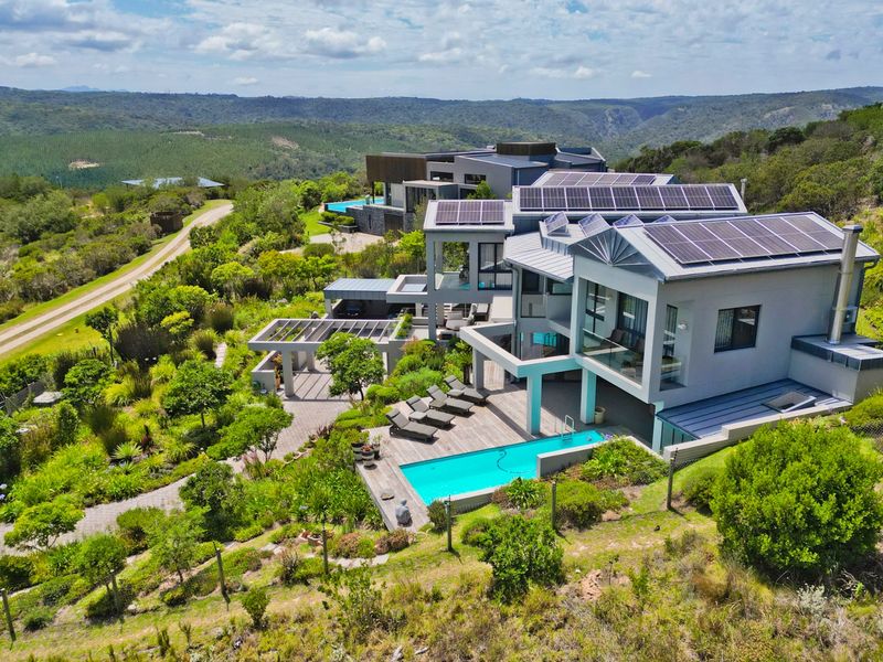 Aerial view of a modern multi-level residence featuring solar panels, a swimming pool, timber decking, and extensive landscaped gardens in a scenic setting.
