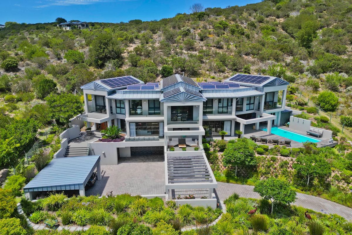 Aerial view of a modern multi-level luxury residence featuring solar panels, a swimming pool, paved driveway, and extensive landscaped grounds.