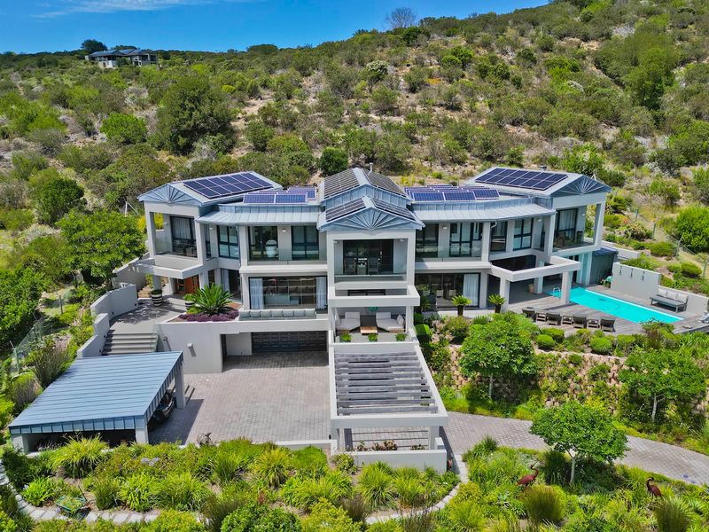 Aerial view of a modern multi-level luxury residence featuring solar panels, a swimming pool, paved driveway, and extensive landscaped grounds.