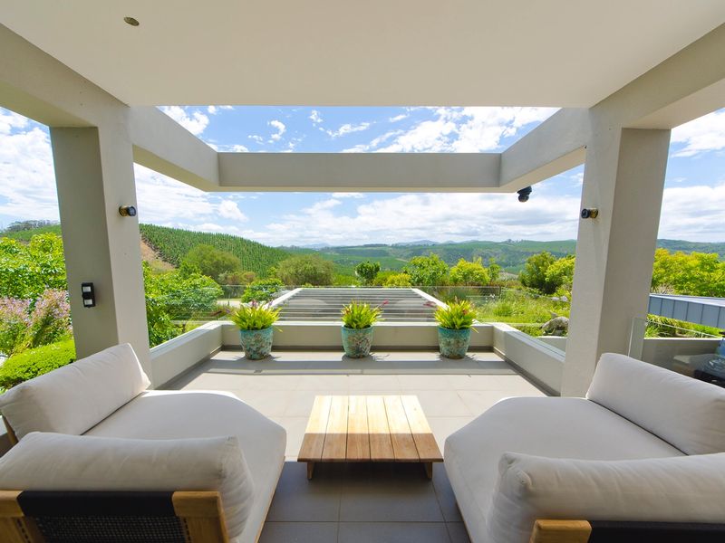 A modern covered patio featuring tiled flooring, a glass balustrade, and expansive views of the surrounding landscape.