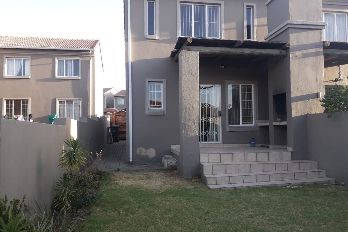 Rear view of the apartment featuring a covered patio with a built-in braai, tiled steps, and a small private garden area.