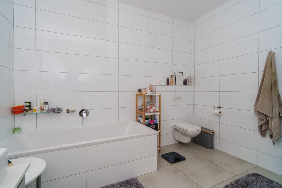 Modern bathroom featuring a built-in bathtub, wall-mounted toilet with concealed cistern, and floor-to-ceiling white wall tiling.