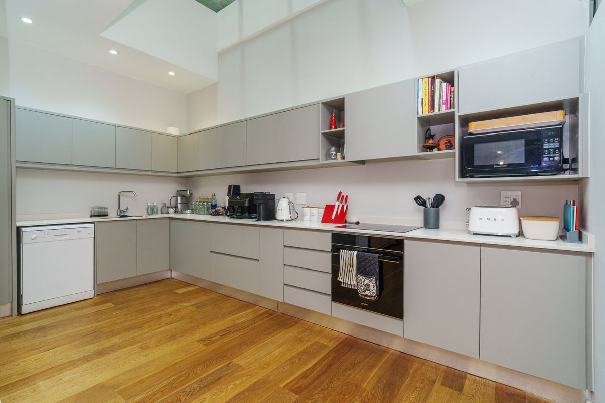 Modern kitchen featuring sleek grey cabinetry, integrated oven, hob, and dishwasher, complemented by warm timber flooring and recessed ceiling lighting.