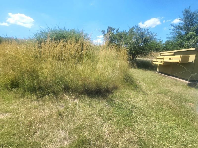A view of a vacant residential plot featuring overgrown grass and a utility transformer box.