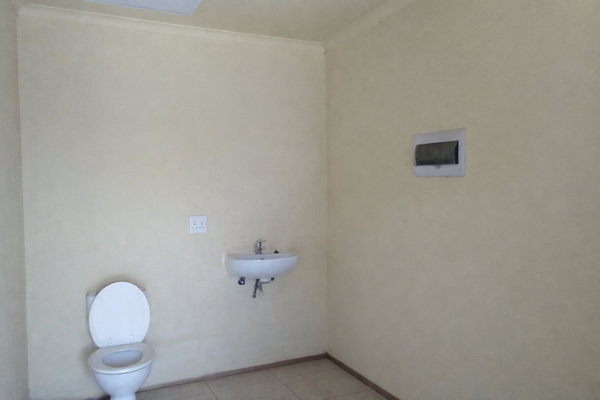 A simple, functional bathroom featuring a wall-mounted basin, a standard toilet, and an exposed electrical distribution board on the wall.