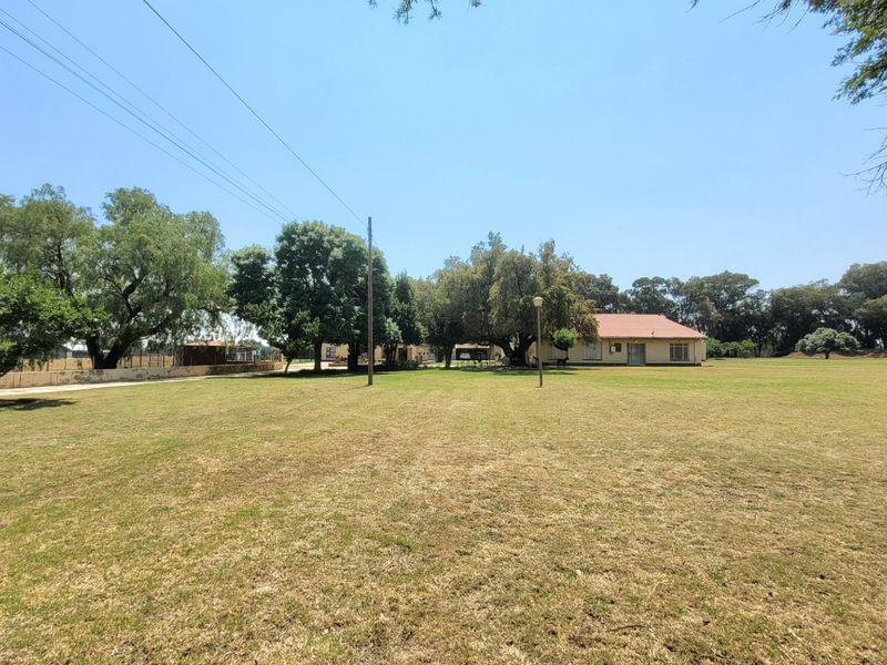 A wide-angle view of the farm property featuring a large, open lawn area, mature trees, and the main residential building in the background.