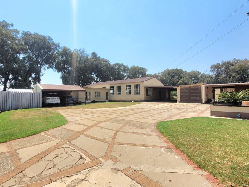 Spacious front exterior view of the farm property featuring a large paved driveway, multiple garage and carport structures, and established lawn areas.