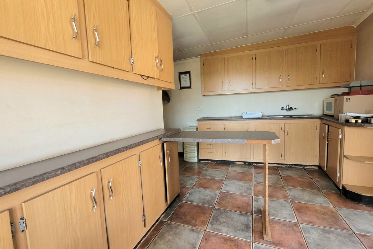 A functional kitchen featuring wood-look laminate cabinetry, tiled flooring, and a breakfast bar extension, offering potential for a modern renovation.