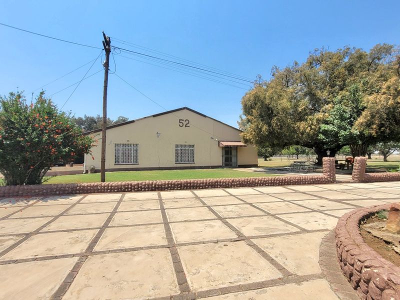Front exterior view of a farm property featuring a paved driveway, stone retaining wall, and a single-story building with security bars.