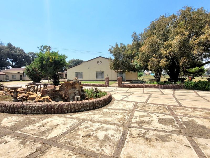 Front exterior view of the farm property featuring a large paved driveway, stone-clad garden feature, and mature trees.