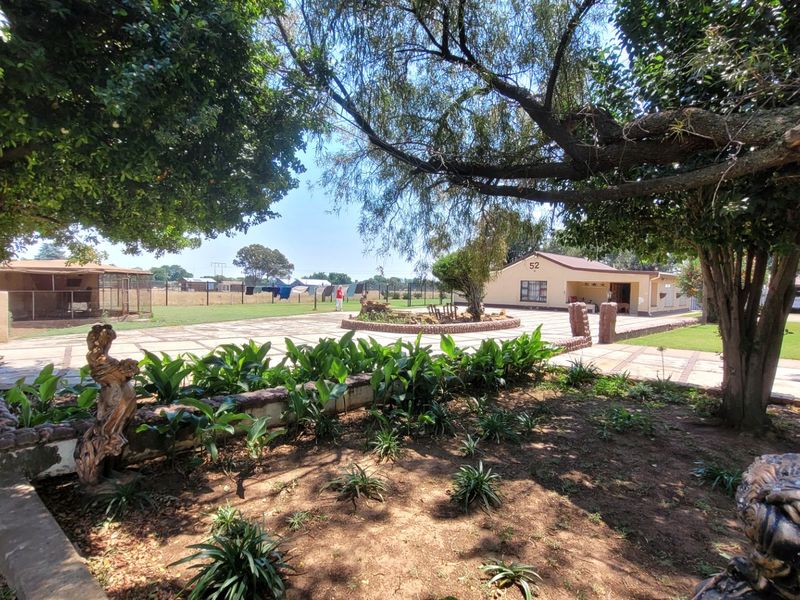 A spacious rear courtyard featuring paved surfaces, established garden beds, and mature trees, providing a functional outdoor area for the farm property.