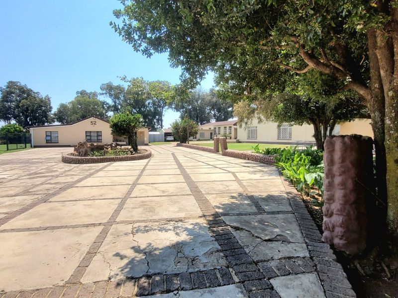 Spacious front exterior view of the farm property featuring a large paved driveway, mature trees, and established garden beds.