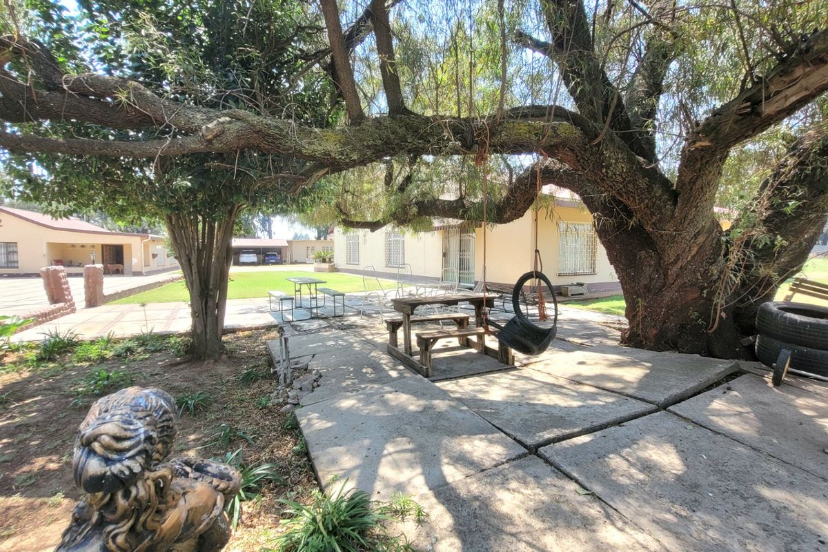 Spacious rear garden area featuring mature trees, concrete paving, and access to the main dwelling with security bars on windows.