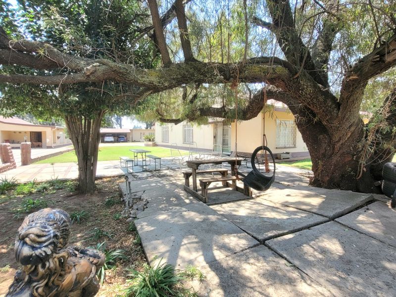Spacious rear garden area featuring mature trees, concrete paving, and access to the main dwelling with security bars on windows.